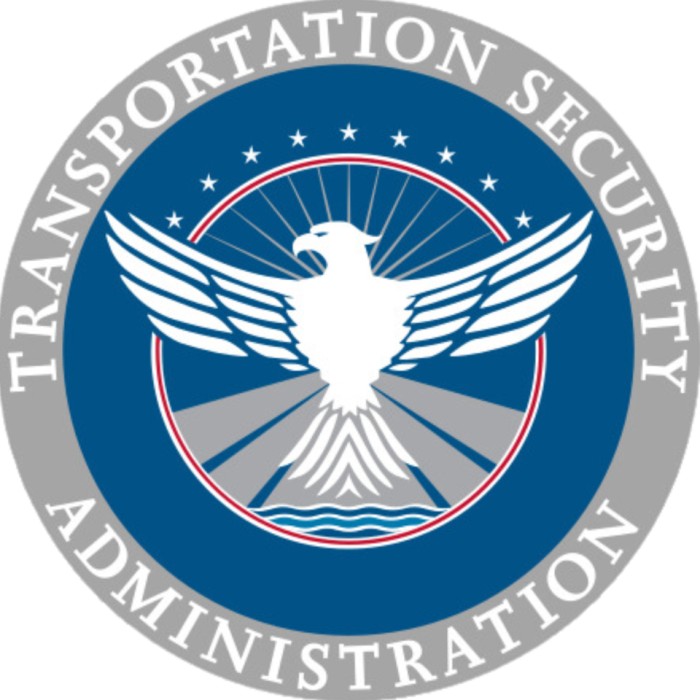 Picture of the TSA Logo in the shape of a circle - the outer part of the circle is gray with white wording that says Transportation Security Administration. The inner portion of the circle is blue with a white bird in the center. There are nine white stars placed above the white bird.